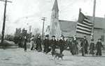 Big Annie Clemenc carries the flag in parade of family members supporting striking miners in Calumet, MI